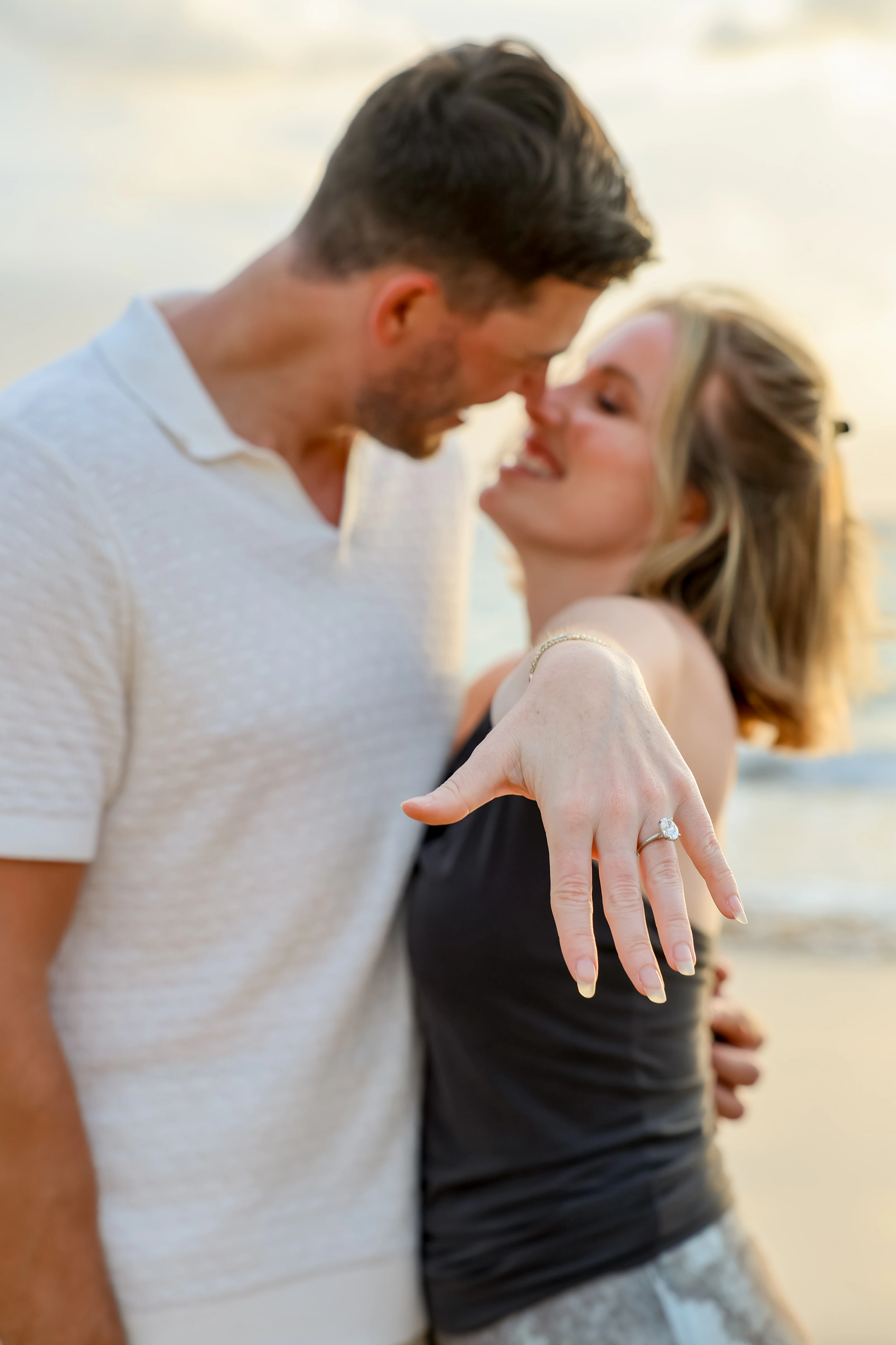 Engaged couple leaning close with a ring held toward the camera