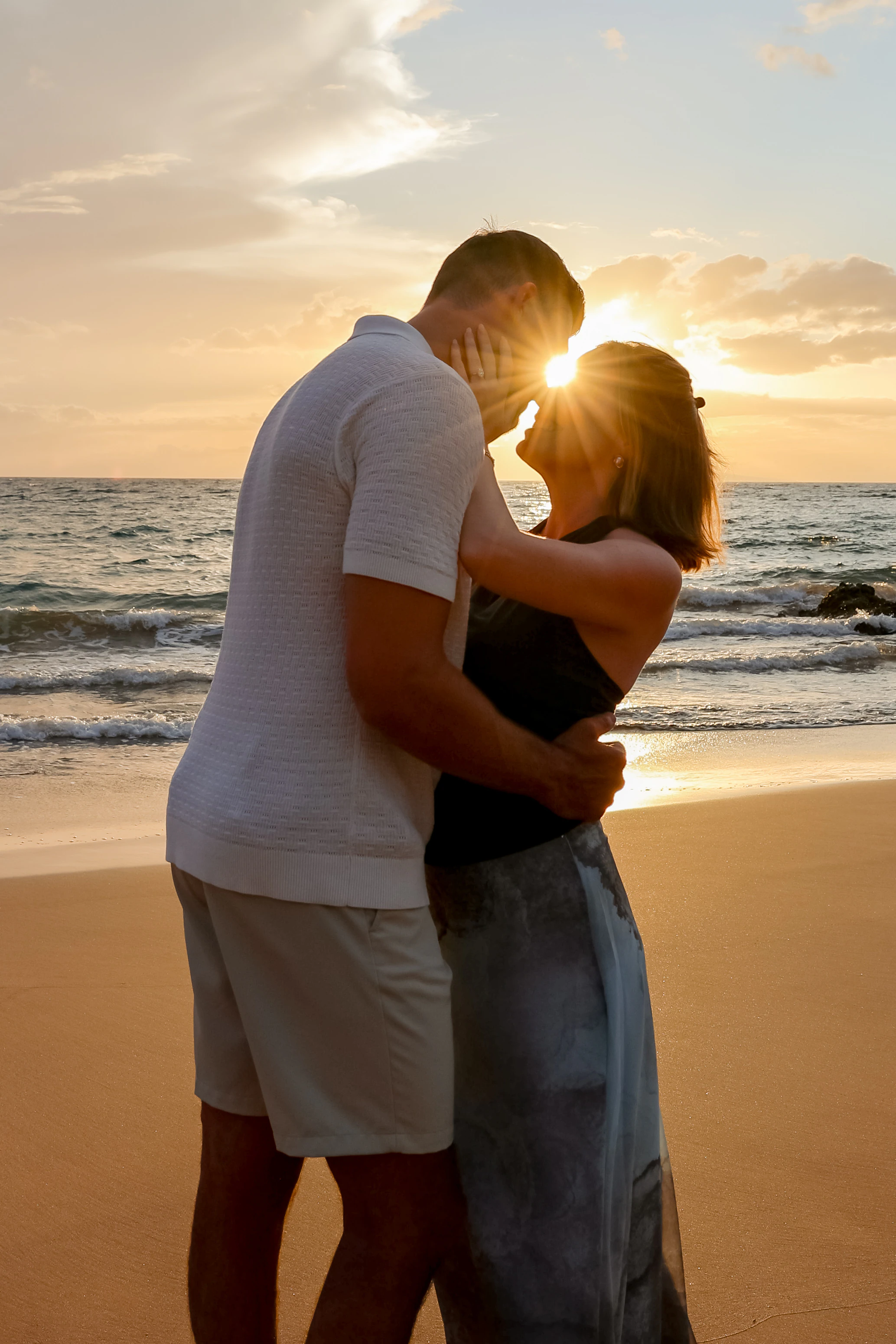 Couple sharing a close moment on the beach with the setting sun between them