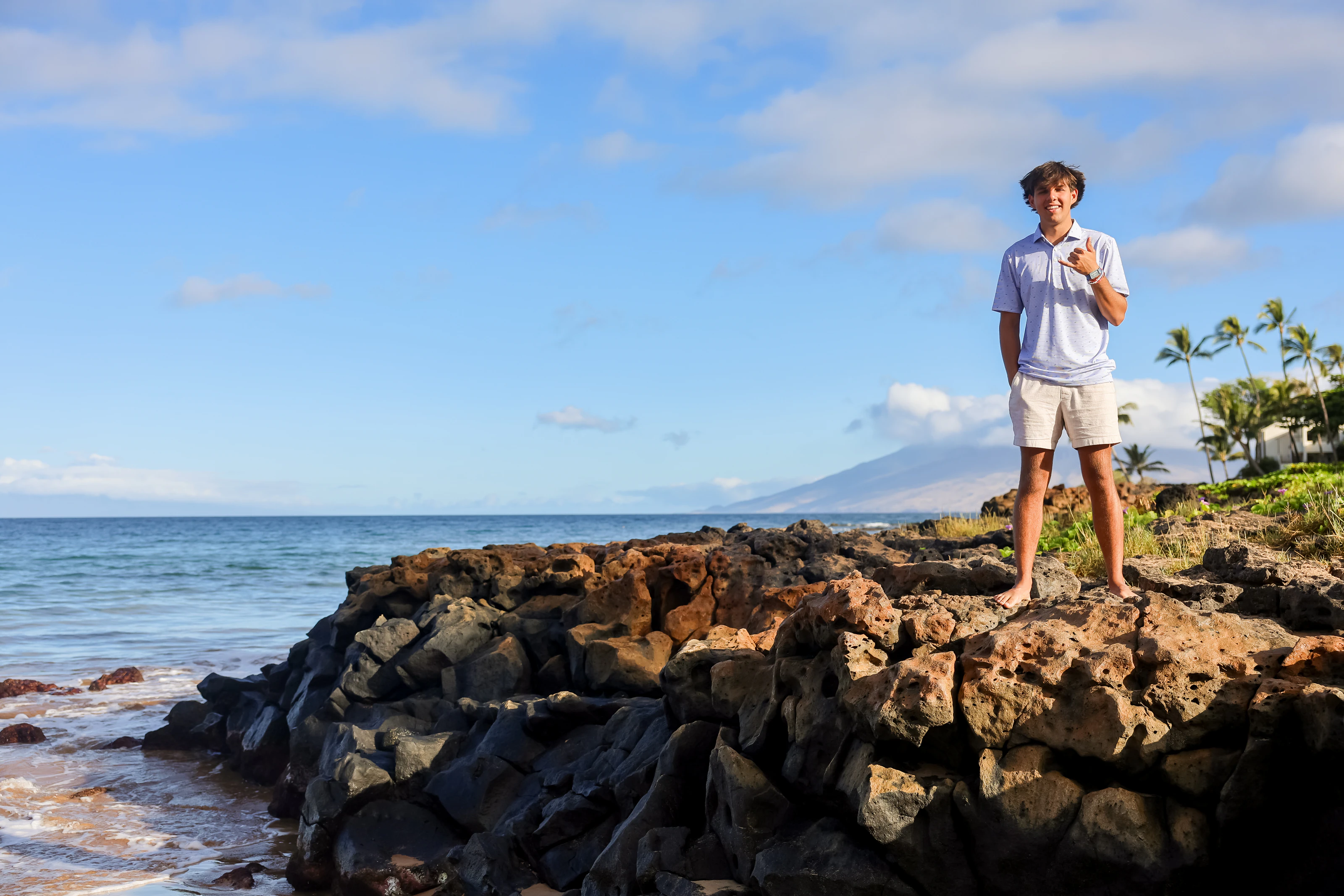 Man giving a shaka from a rocky Maui shoreline with ocean and open sky
