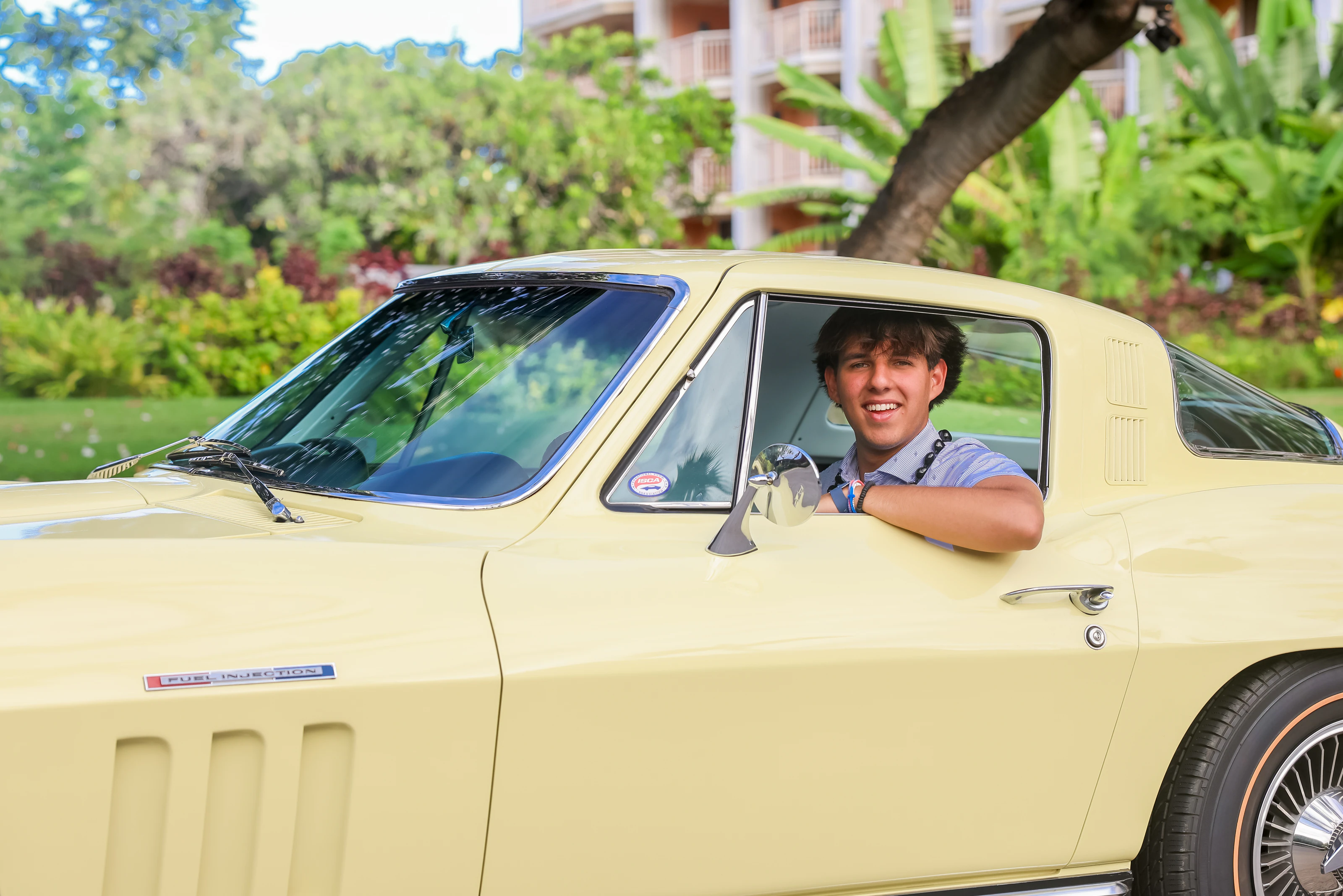 Smiling man leaning from the driver's window of a pale yellow classic car