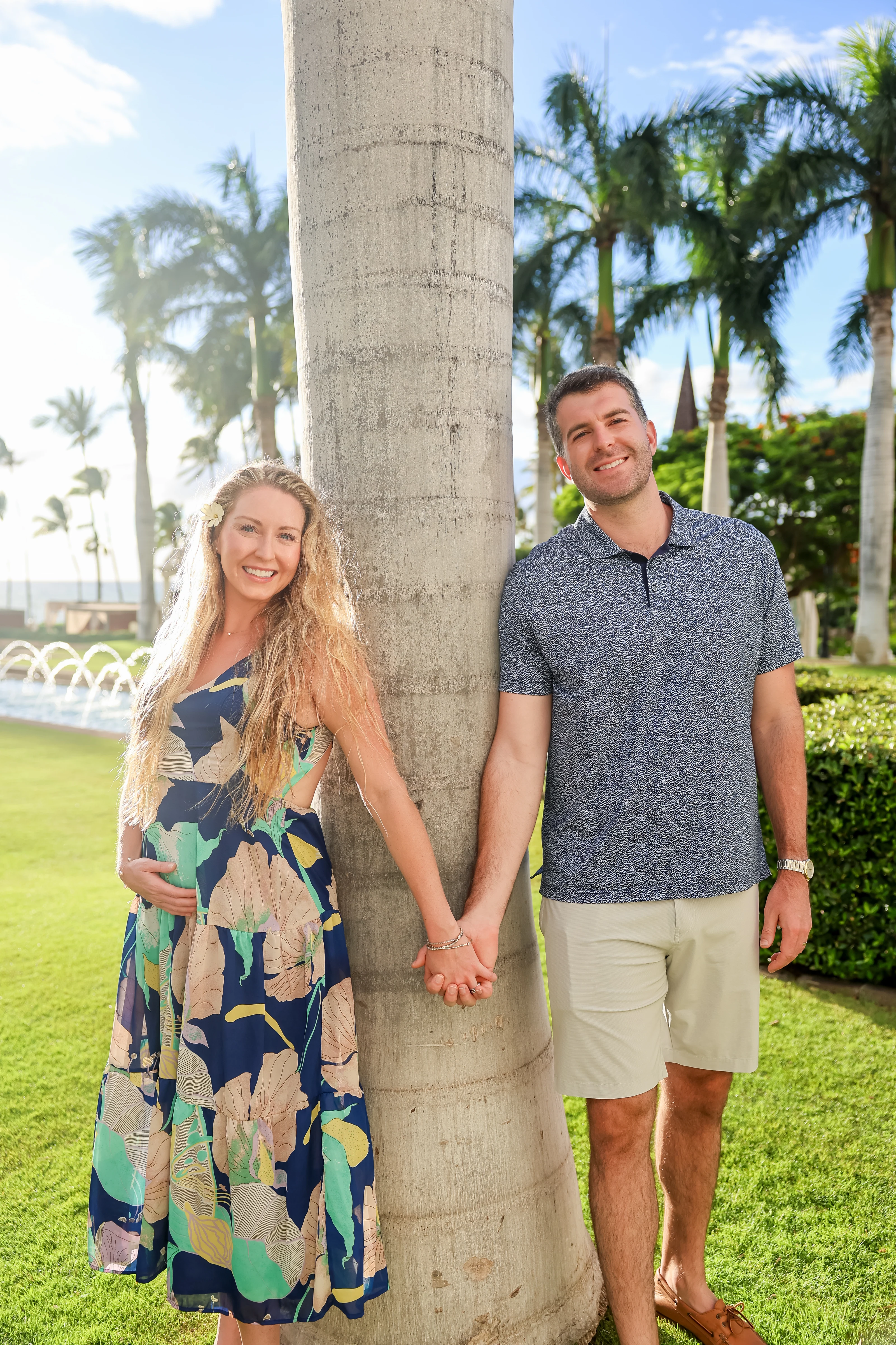 Expectant couple holding hands around a palm tree