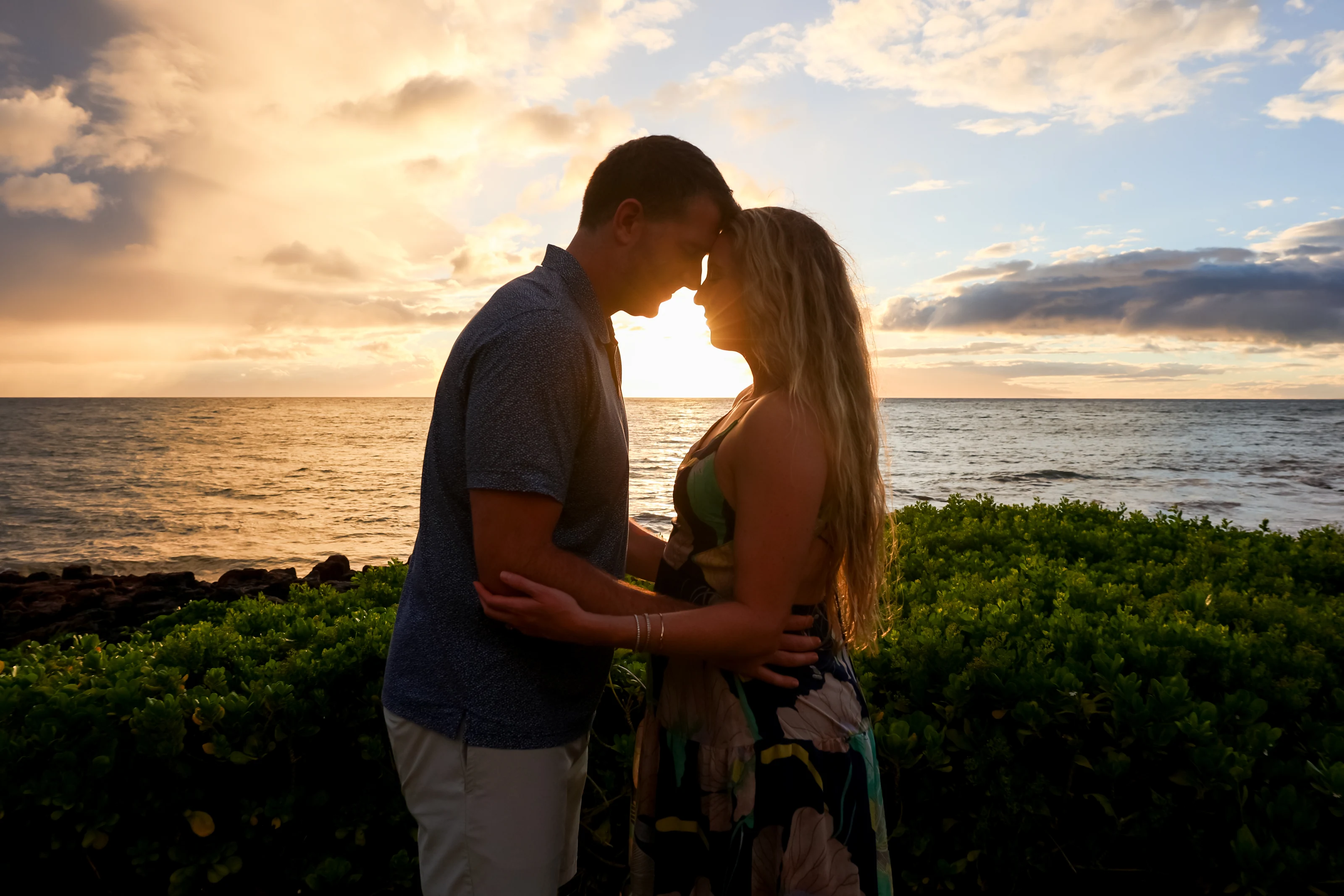 Couple touching foreheads beside the ocean in golden sunset light