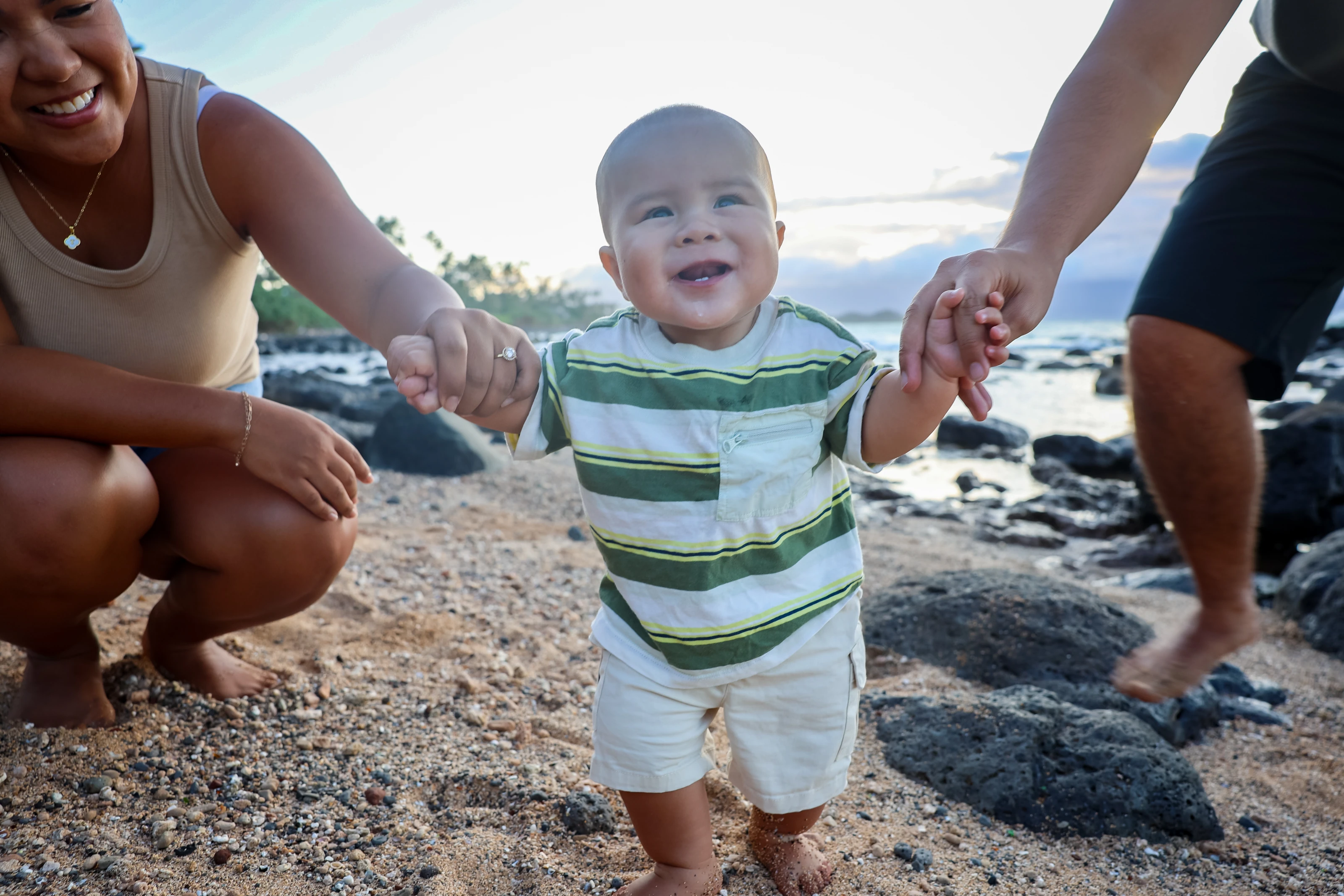 Baby taking steps with both parents at the Maui shoreline