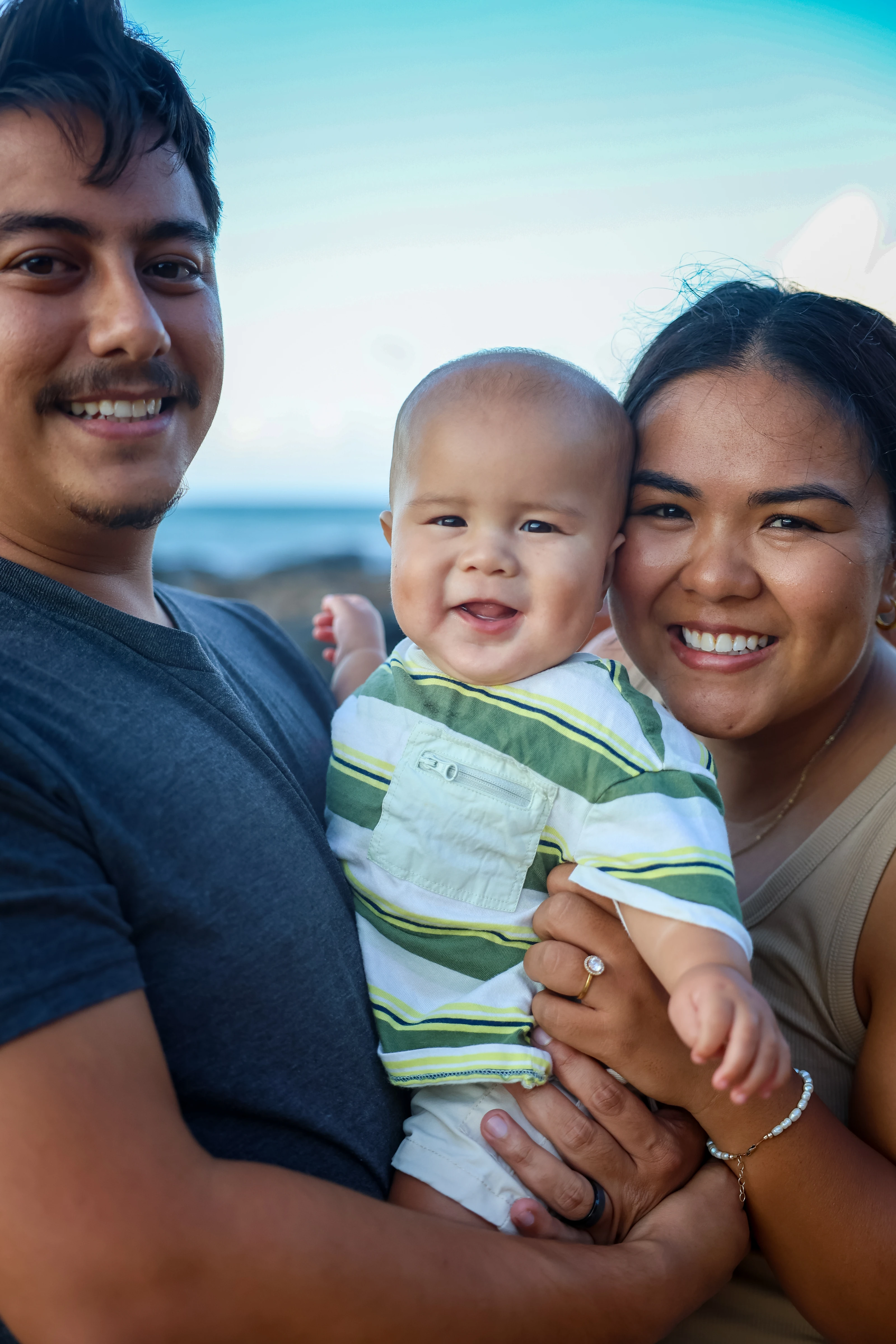 Parents cuddling their baby for a close family portrait by the ocean