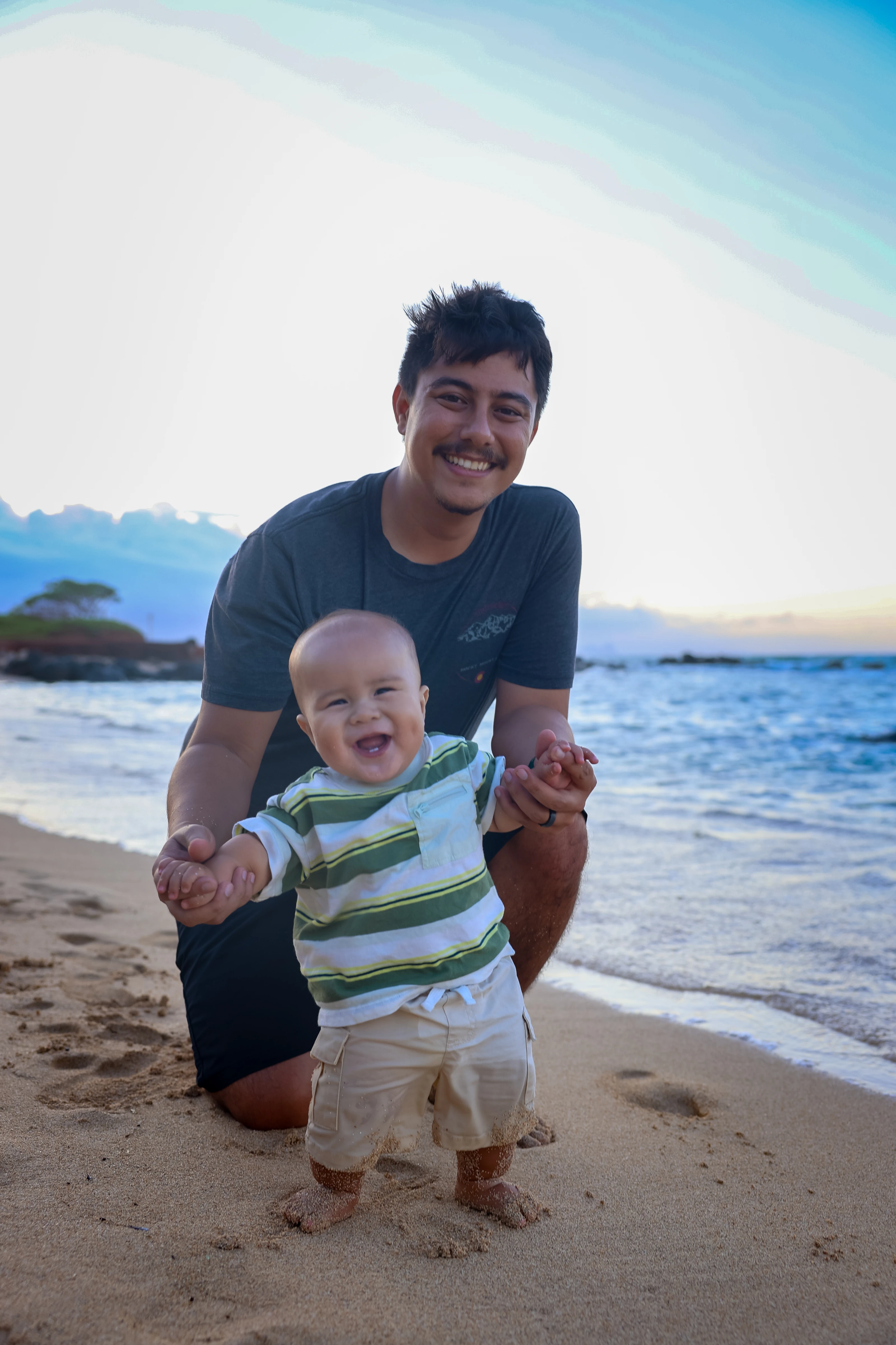 Father helping his smiling baby stand on a Maui beach
