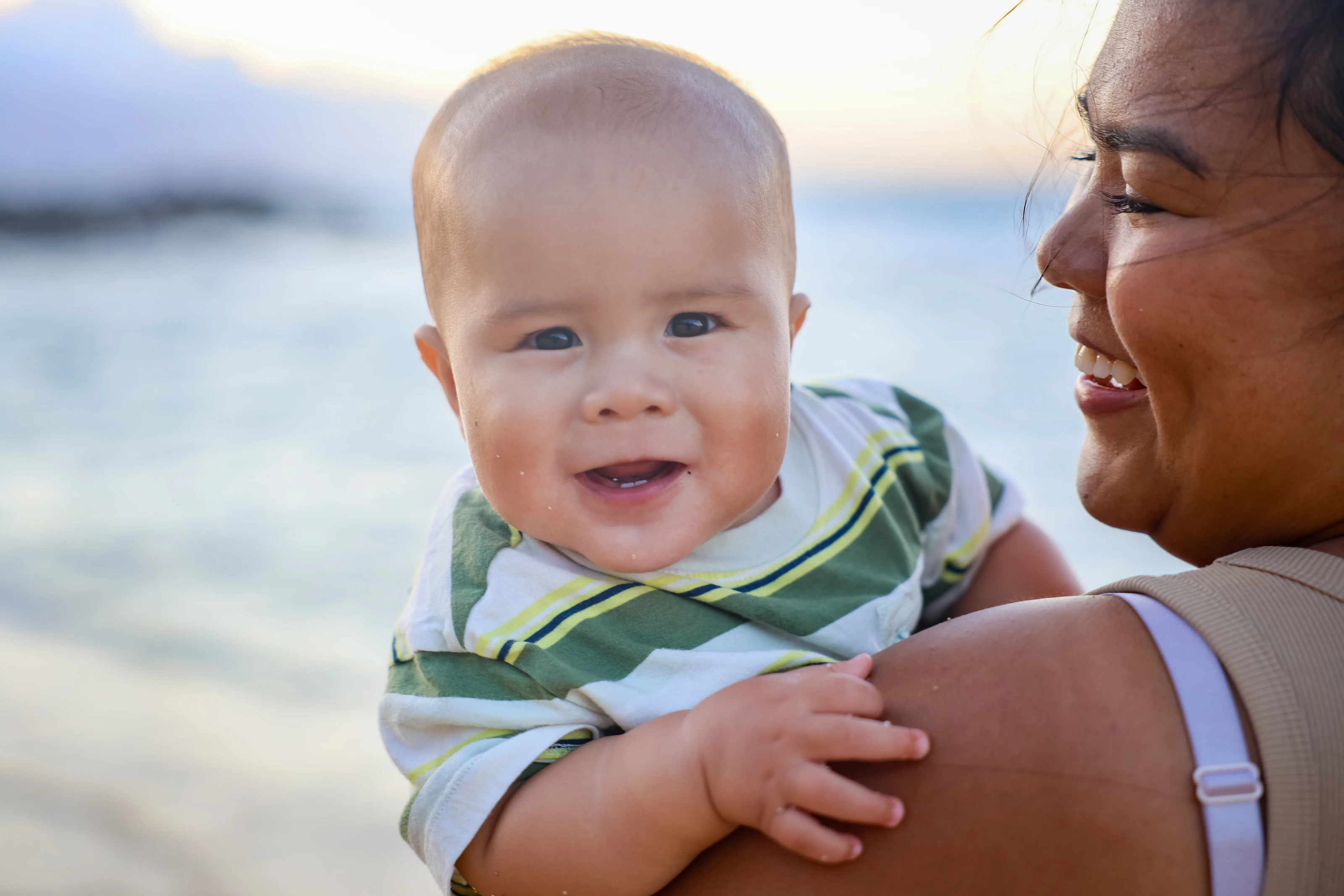 Smiling baby held by their mother beside the ocean in Maui