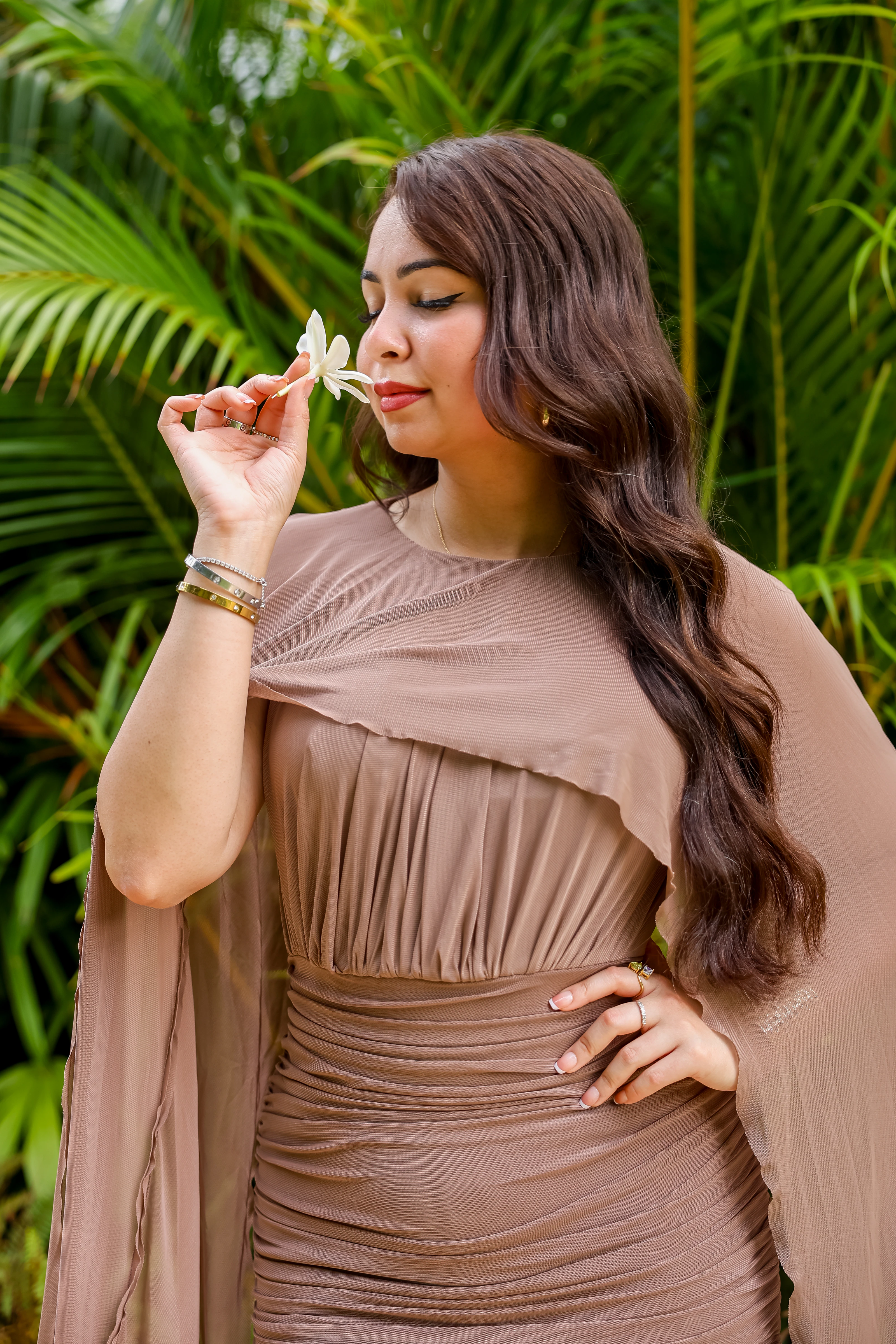Woman in a brown dress holding a white flower in a tropical garden