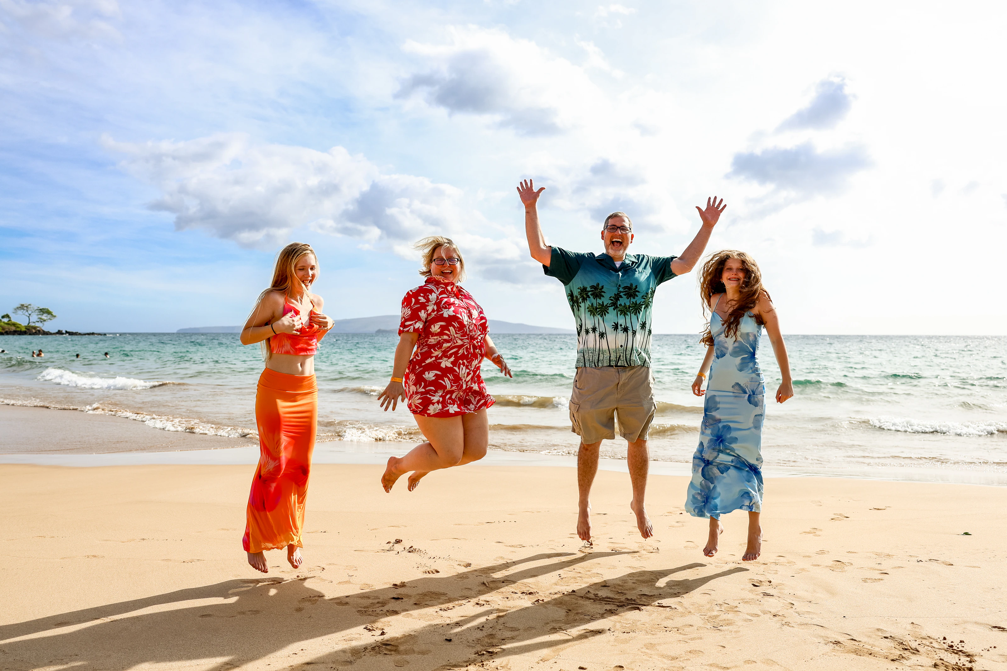 Family of four jumping on a Maui beach in bright sunlight