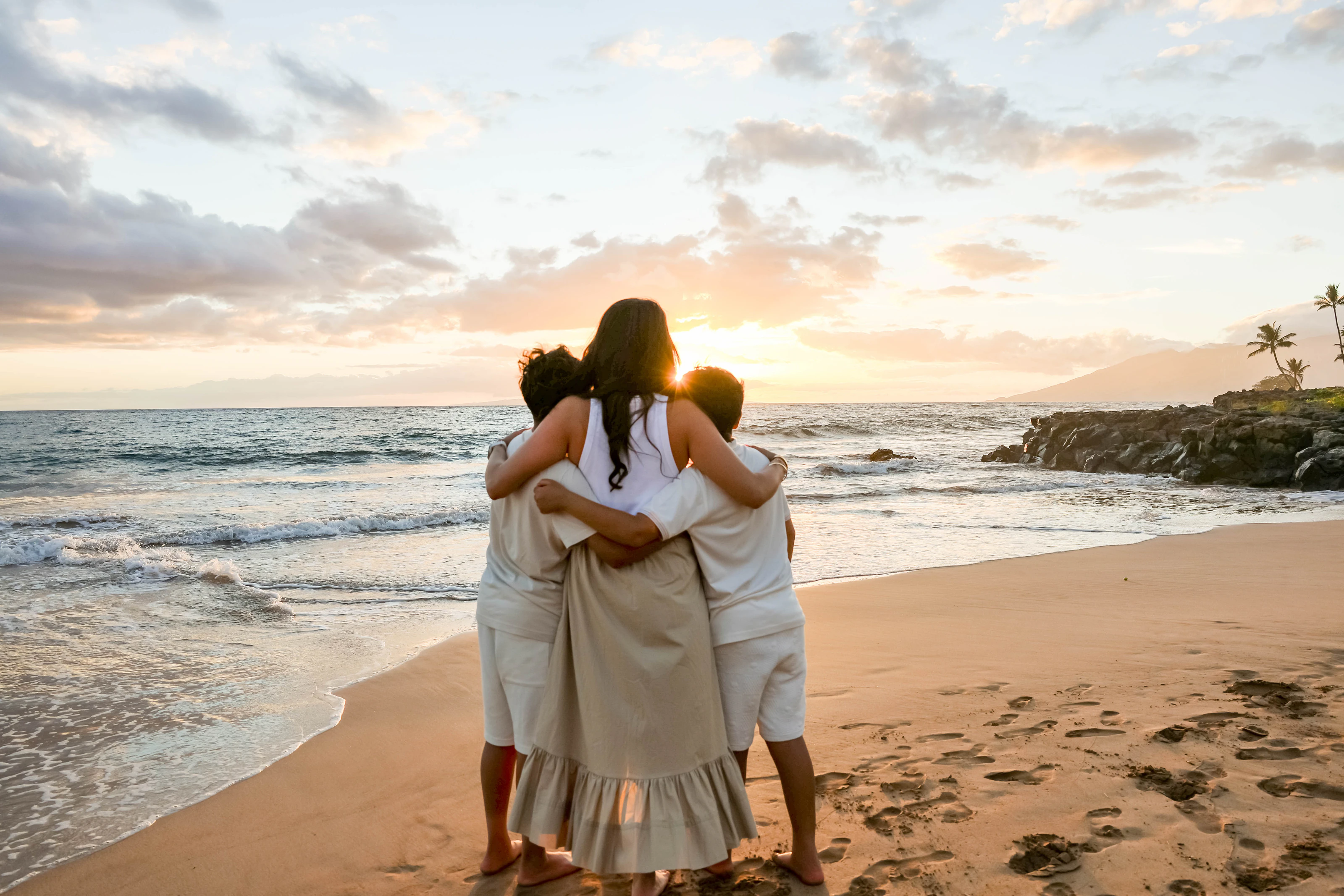 Family embracing from behind on a Maui beach at sunset