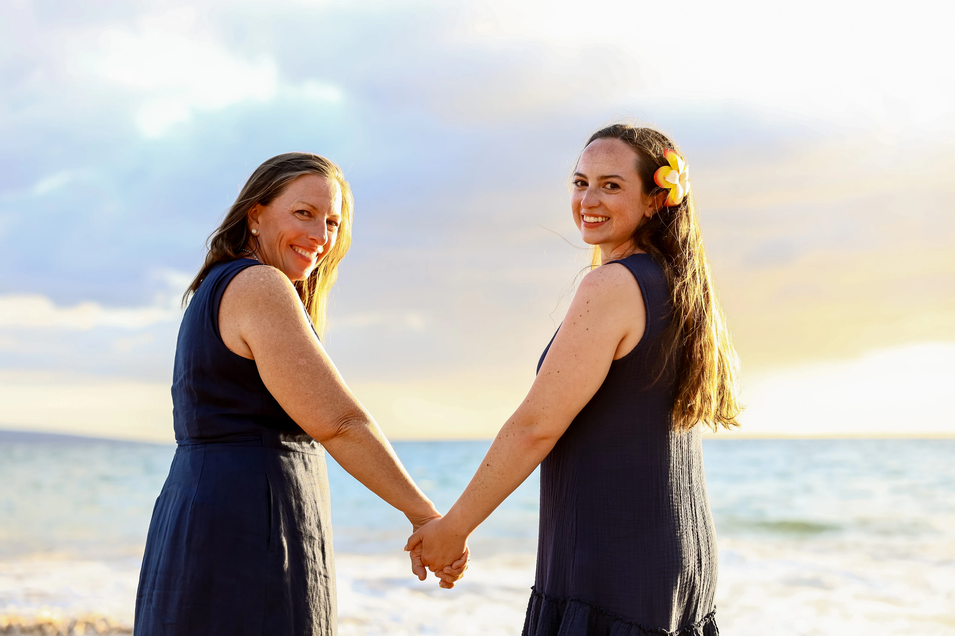Two women in navy dresses holding hands at golden hour