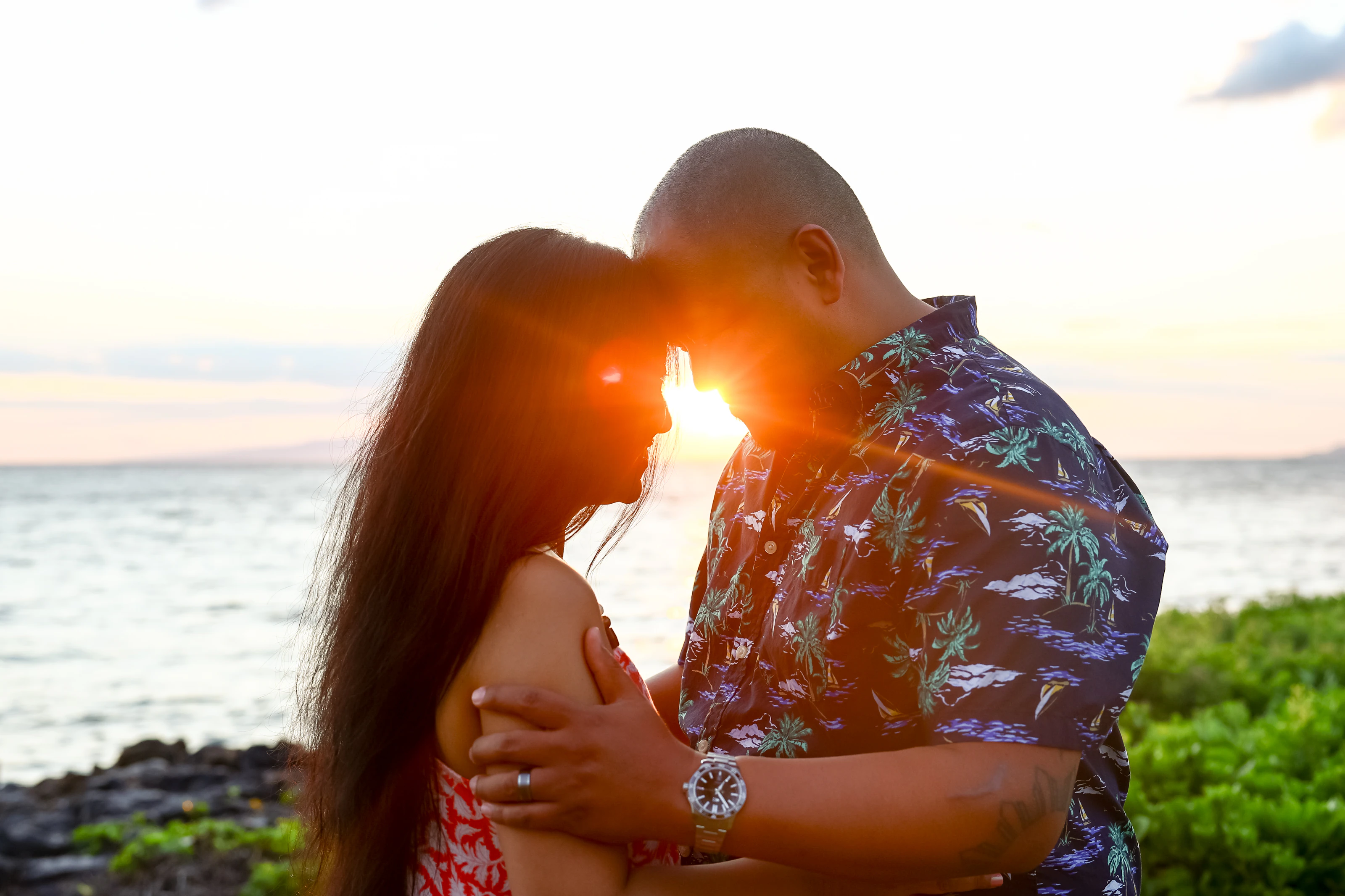 Couple touching foreheads beside the ocean with sunset light between them