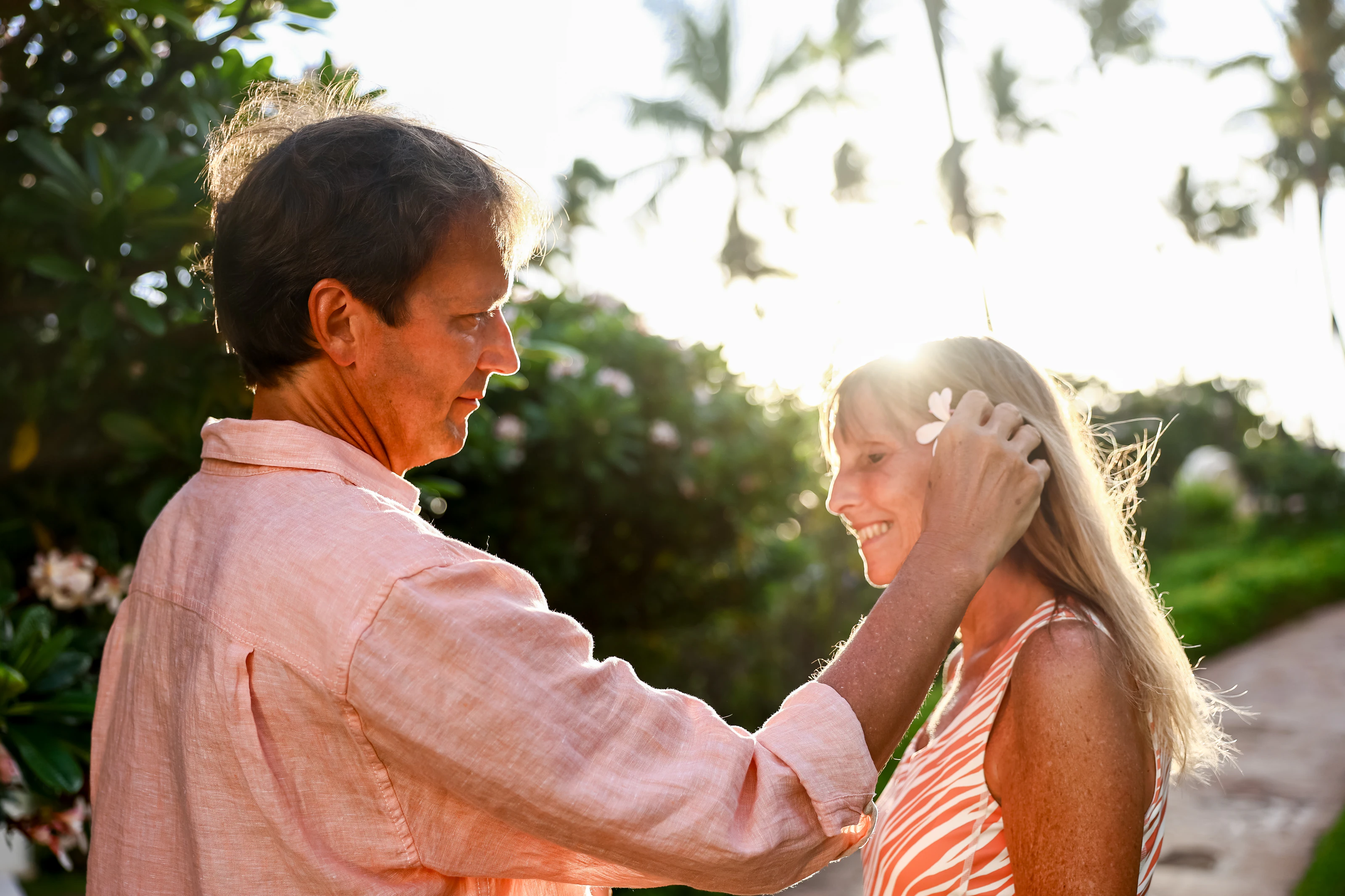Man tucking a plumeria flower behind a woman's ear in warm evening light