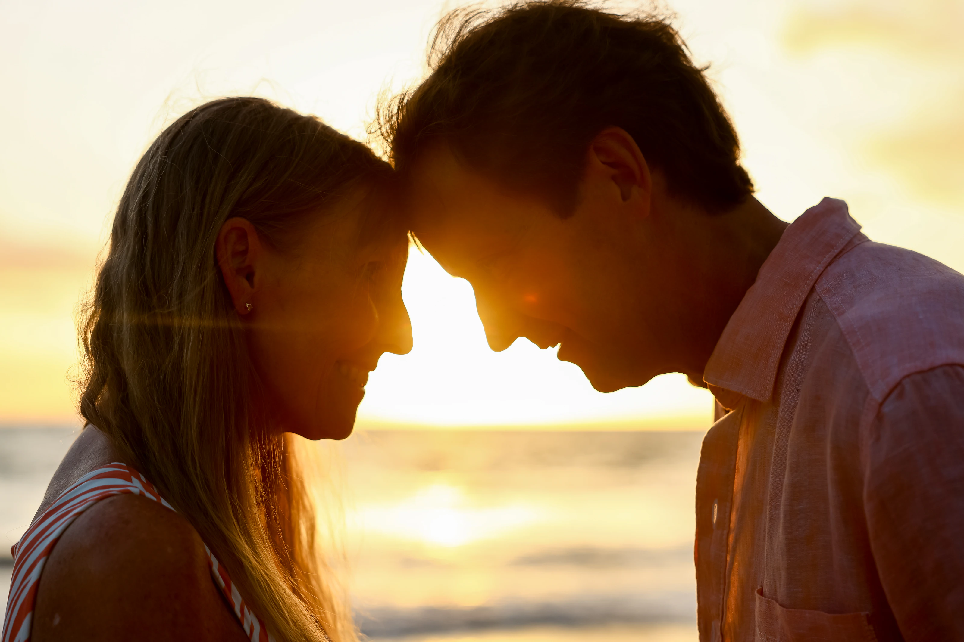 Close silhouette of a couple touching foreheads with the sunset between them