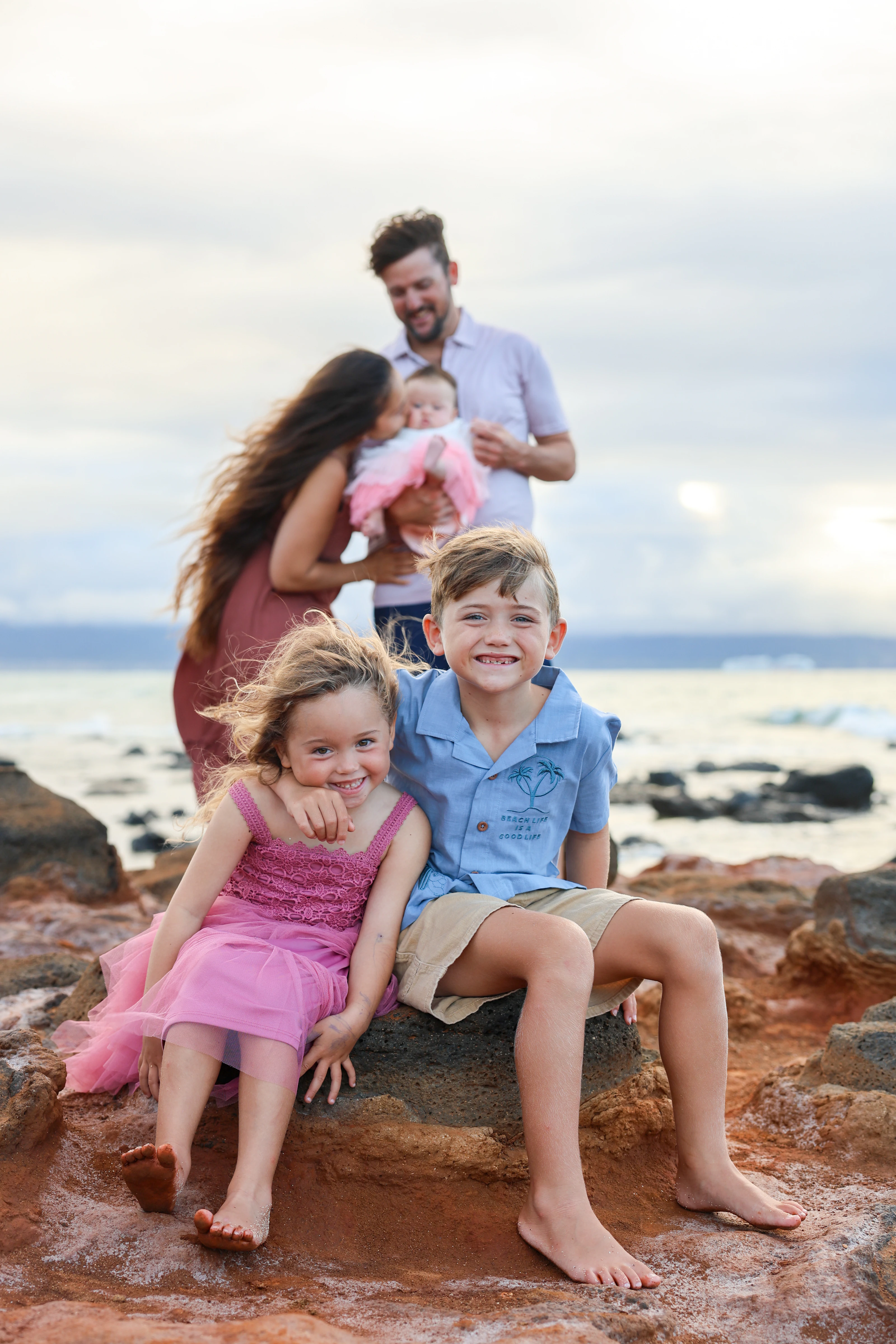Two siblings sitting together while their family shares a moment behind them