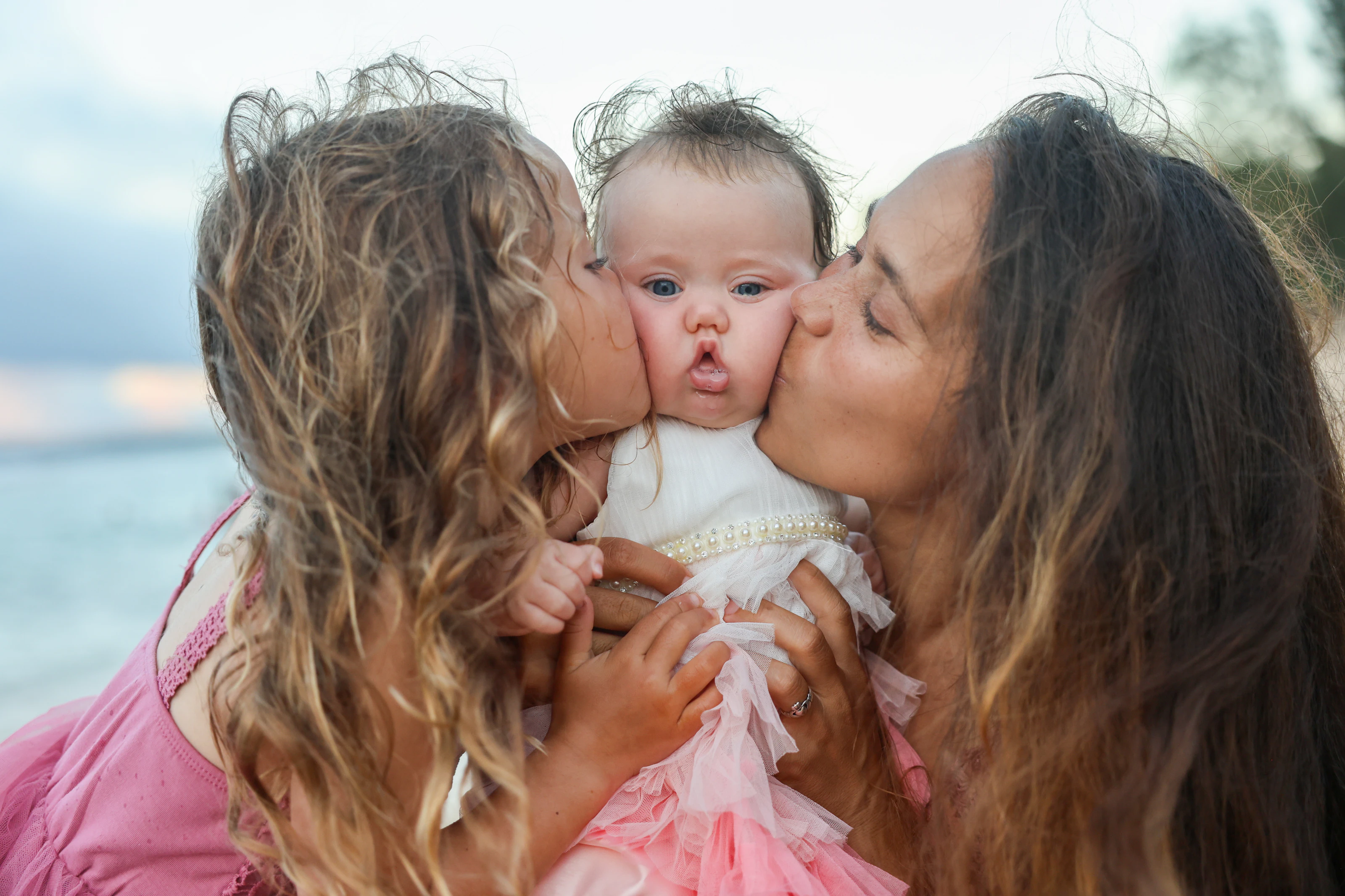 Two family members kissing a baby on the cheeks beside the ocean