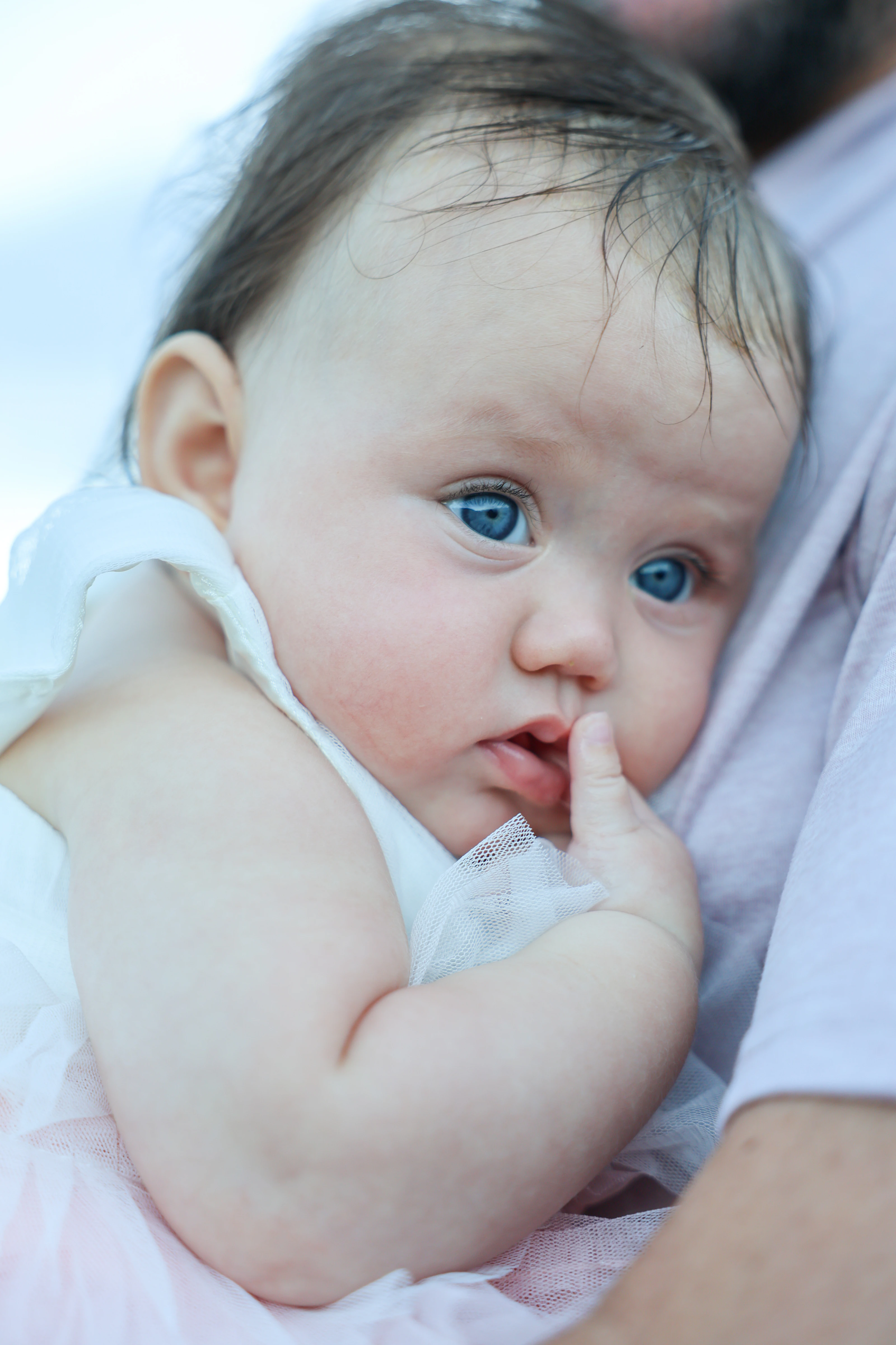 Close portrait of a baby resting against a parent