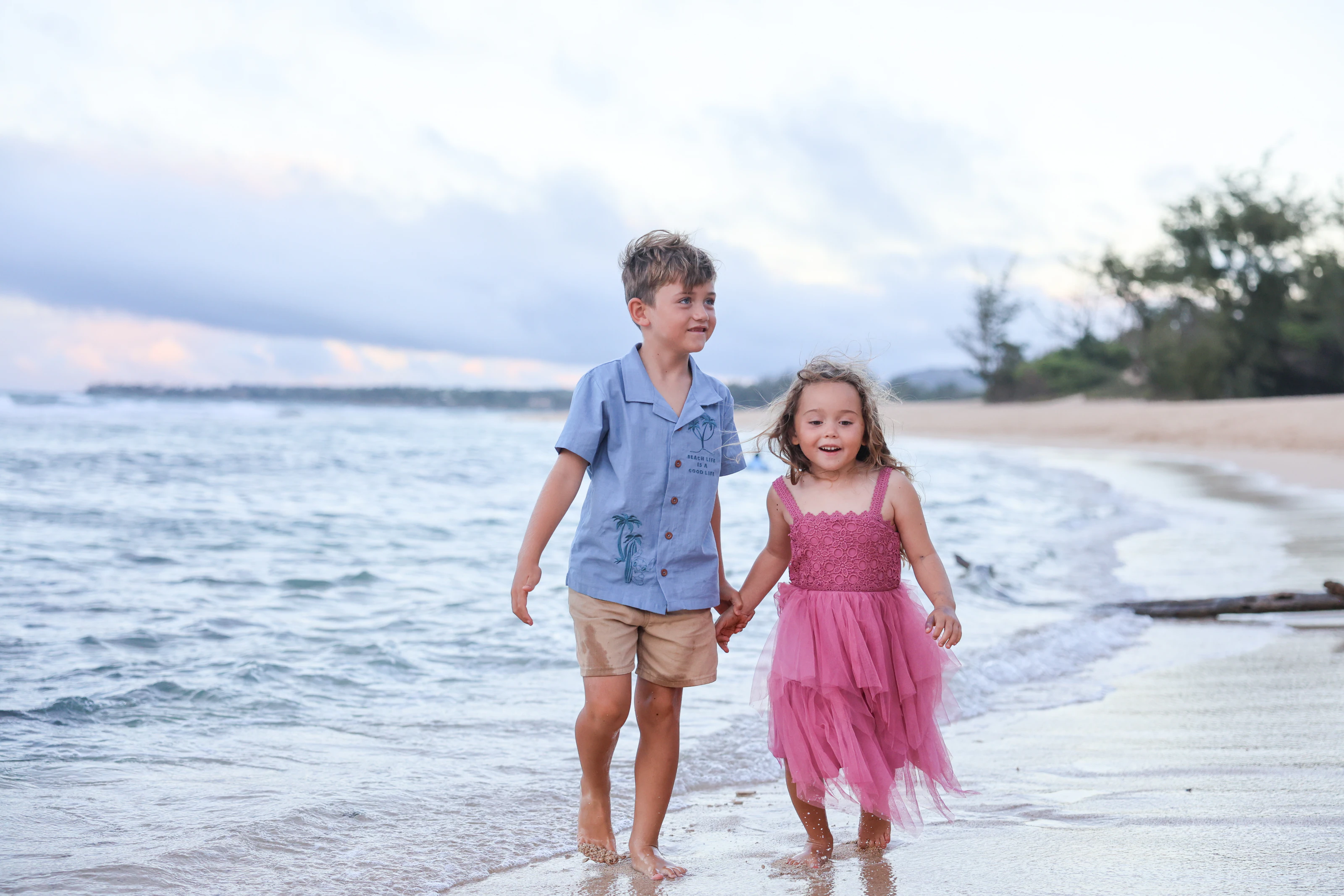 Siblings holding hands in shallow ocean water