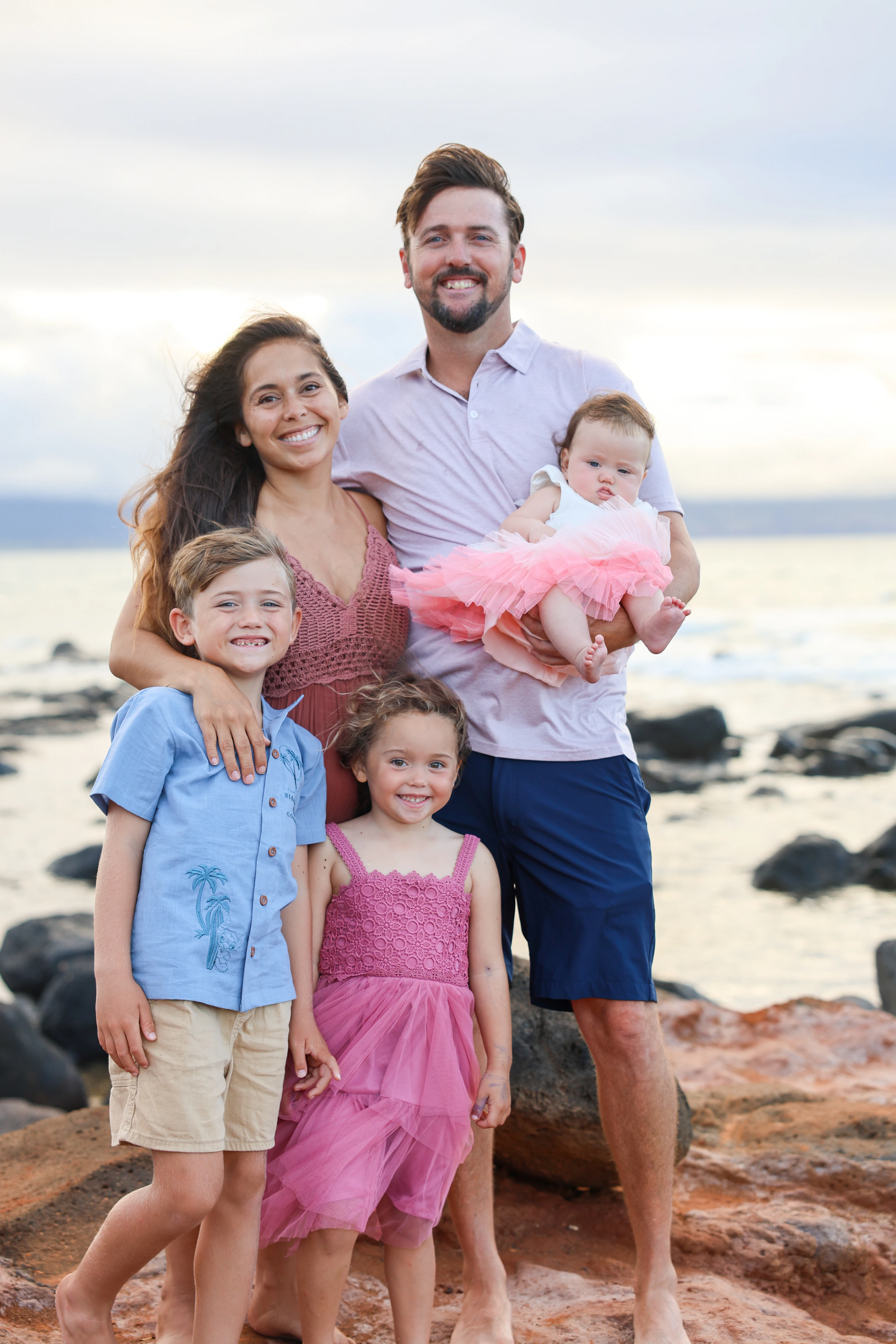 Family of five smiling together on a rocky Maui shoreline