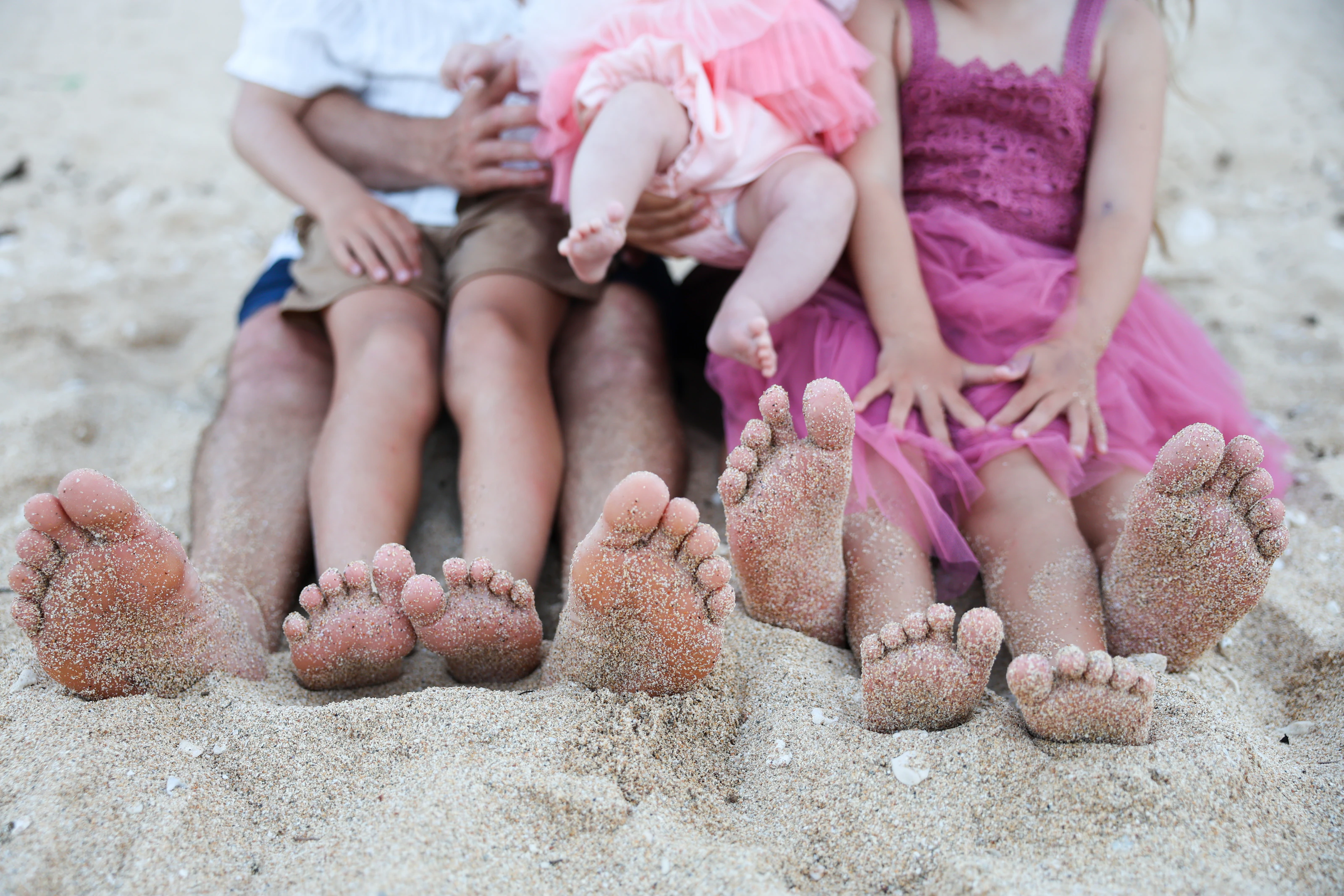 Family feet in the sand with children seated behind