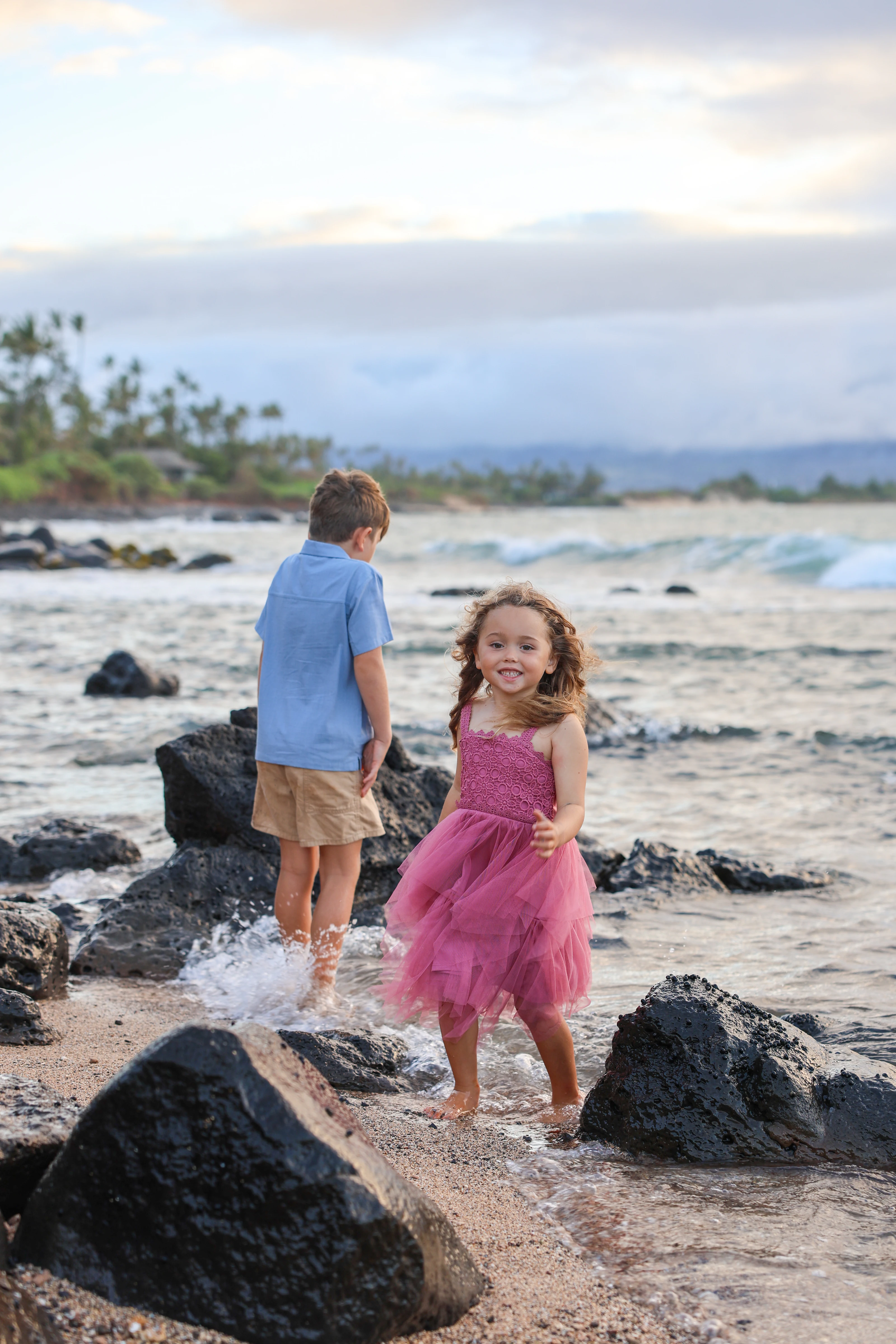 Two children playing among lava rocks by the ocean