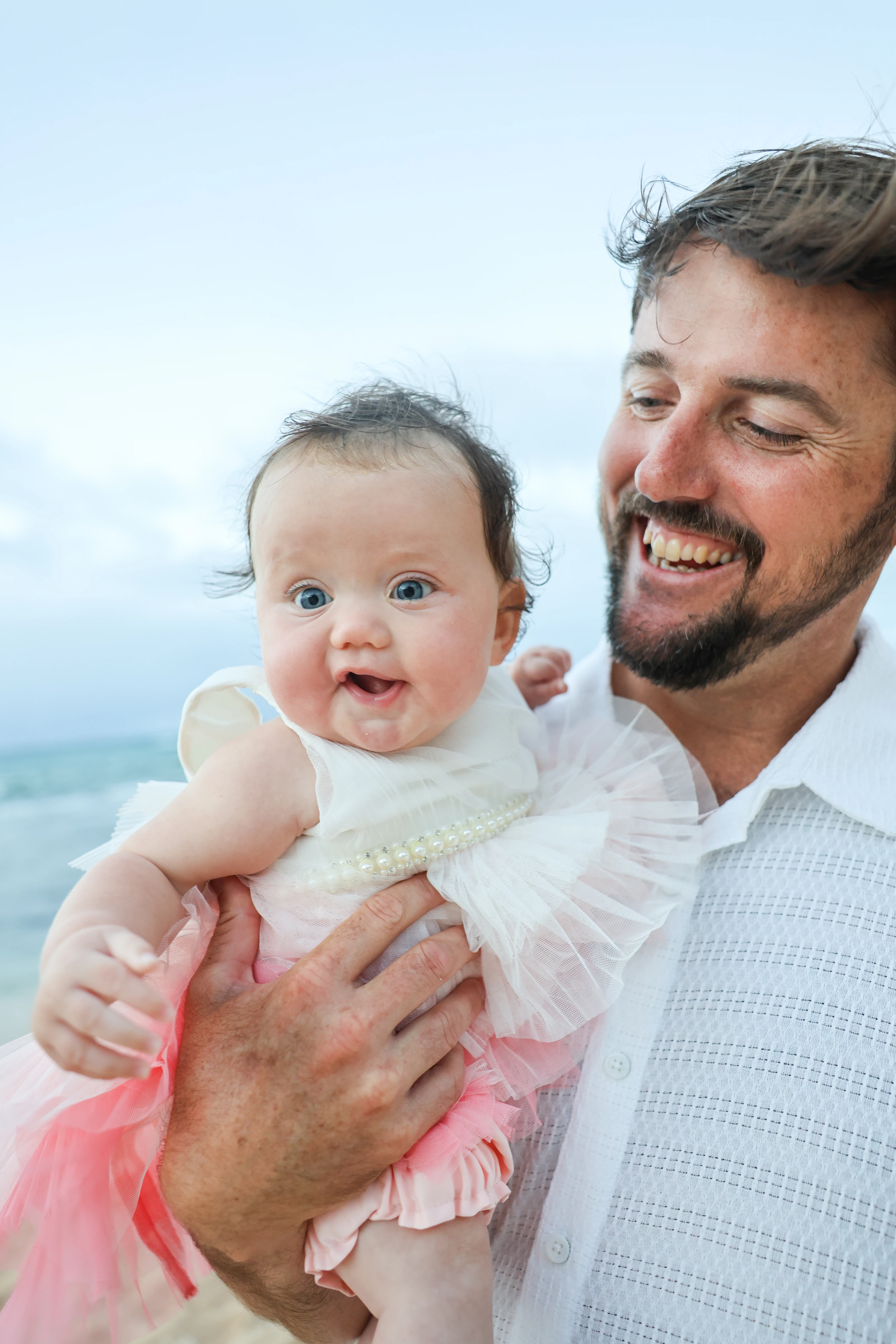 Parent holding a smiling baby beside the ocean